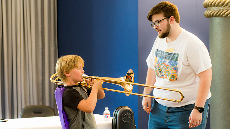 Image of musical teacher guiding student on the trombone
